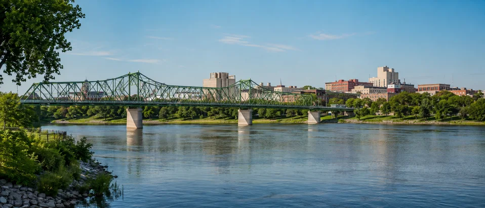 Green steel truss bridge crossing the calm Red River toward downtown Grand Forks in summer